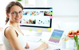 A woman with glasses works on her computer at a desk, representing the Adobe Behance Online Course.