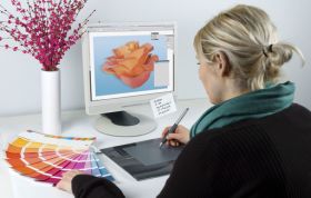 A woman with a paintbrush engages with a computer, illustrating digital design, representing the Adobe Dreamweaver Online Course.