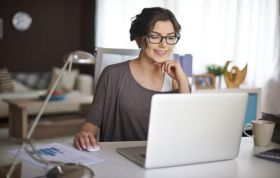A woman wearing glasses sits at a desk, focused on her laptop, representing the Adobe Spark Online Course.