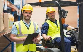 Two men in a factory, one with a board and pen, another in a forklift, representing Articulated Forklift Truck Operations and safety.
