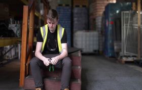Young man seated on warehouse stairs in dim lighting, representing the Bullying & Harassment for Managers Online training course.