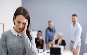 Stressed woman holding her head in a meeting room, representing the Bullying and Harassment for Employees awareness and training course.