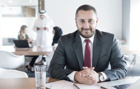 A smiling man in a suit and tie, exuding warmth, representing the CAPM Online Course.