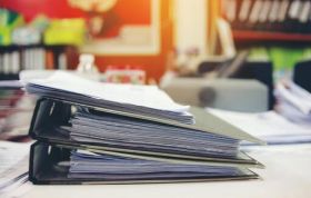 A stack of papers on a desk, symbolizing organization, representing the Care Planning & Recording Keeping Online course.