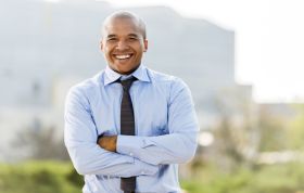 Smiling Black man in blue shirt and tie, exuding confidence, representing the CCNA Security Course for network security skills and certification.
