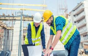 Two construction officers reviewing plans on a laptop at a site, representing CDM Awareness and safety in the construction industry.