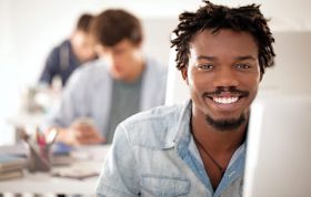 A smiling man sits at a computer, engaged in his work, representing the Certified Blockchain Developer Hyperledger Online Course.