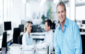 Man in blue shirt standing calmly by desk, representing the Certified Information Security Manager CISM course for leadership in information security.
