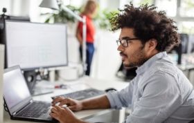 A man wearing glasses focuses on his laptop, representing the Certified Kubernetes Administrator (CKA) Online Course.