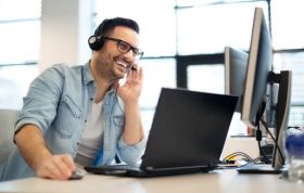 A man with headphones smiles while working on a computer, representing the Certified Kubernetes Application Developer Online Course.