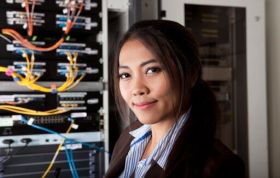 Woman in business suit stands confidently by server rack, representing the Cisco CCNA Course in a professional tech environment.
