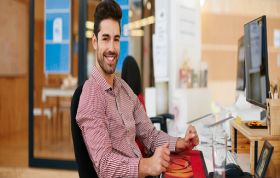 Man sitting at desk with hands raised, looking excited, representing the Cisco CCNA Voice Course for voice network technologies and certification.