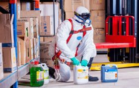 Man in PPE using cleaning materials to manage spills, representing Cleaning and Containing Chemical Spills and handling dangerous substances.