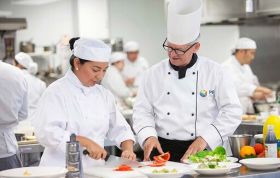 Chefs prepare dishes in a commercial kitchen, representing the Compliance Training for Kitchen Staff course.