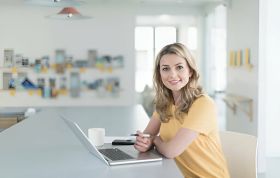 A woman focused on her laptop in a bright office, representing the CompTIA CASP Course.