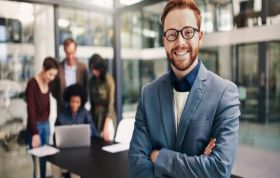 Man standing confidently with colleagues working behind, highlighting professional skills from the CompTIA Data+ course.
