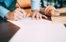 Two individuals sign documents together, emphasizing collaboration for the Contracts and Written Statements Online Course.