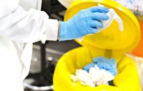 Man in PPE using a bin for dangerous materials, highlighting COSHH Interactive course and proper handling of hazardous substances.