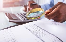 Businessman uses magnifying glass to review documents, highlighting detail focus for Counter Fraud in the NHS Online Course.