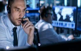 Man wearing headset looking at monitor with colleague behind, representing CySA+ training and understanding the cybersecurity framework.