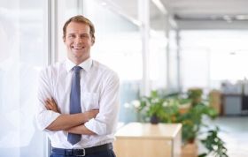Man in business suit standing confidently in a modern office, representing the Designing Business Intelligence Solutions with SQL Server course.