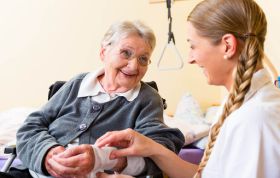 A nurse supports an elderly woman in a wheelchair, symbolizing care in the Dignity and Respect Online Course.