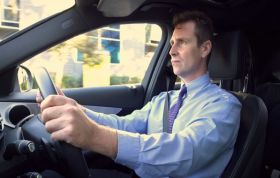 Man in blue shirt and tie driving attentively, representing the Driver Safety Interactive Online Course with a focus on safe driving habits.
