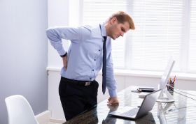 Man in office holding his lower back in discomfort, illustrating poor posture, representing the DSE Workstation Assessment Online course.