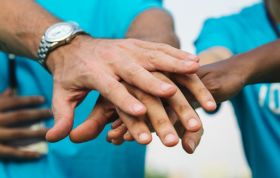 A diverse group joins hands in unity, symbolizing teamwork and support, representing the Duty of Care Online Course.