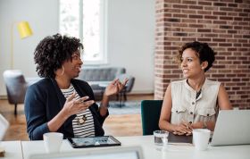 Two women talking at a desk, highlighting Effective Communication and the ability to communicate effectively in the workplace.