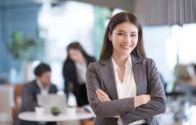 Well-dressed woman standing with team in background working on laptops, representing Blockchain Solutions course for solutions engineers.
