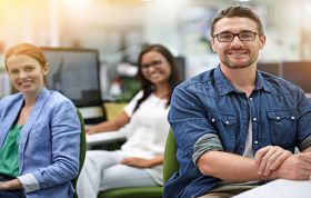 Man at his desk with two colleagues behind him, representing the Facebook 101 course for beginners learning Facebook basics and tools.