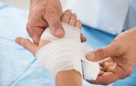 A doctor wraps a patient's hand with bandages, representing the First Aid Burns Online course for protection and support.