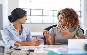 Two women conversing at a desk in an office, representing the Giving and Receiving Feedback Online Course.