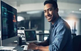 Smiling man working on computer at desk, representing Google Cloud Digital Leader course and preparation for Cloud Digital Leader exam.