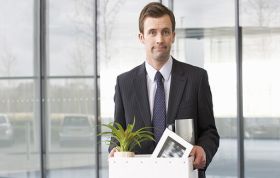 A man in a suit holds a box with a small plant, smiling, representing the Handling Redundancy Online course.