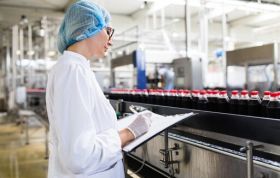 Woman in lab coat oversees conveyor belt in lab representing Health and Safety in a Food Environment Online course