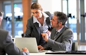 Man and woman discussing information on a laptop, emphasizing Information Governance and the source of information in a workplace setting.