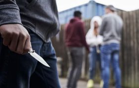 Man holding a knife while two others attack a person, representing Knife Crime Awareness and understanding the impact of knife crime.