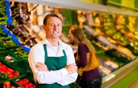 Cheerful man poses by fresh produce, representing the Level 2 Food Safety for Retail Online course with vibrant fruits and vegetables.