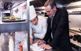Person showing paper to chef in kitchen, representing Level 2 HACCP course for food businesses and ensuring food safety standards.