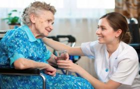 Female staff assisting elderly disabled woman, representing Control and Administration of Medication course in social care environments.