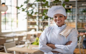 A smiling woman in a chef hat, exuding joy in a culinary setting, representing the Level 3 Food Safety for Catering Online Course.