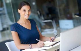 Woman seated at tidy desk with pen in hand, focused on laptop, representing the Managing and Maintaining Windows 8 Online Course.