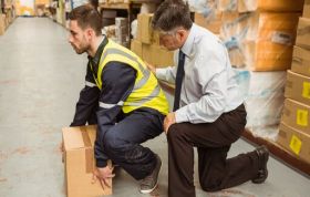 Man in uniform lifting a box with boss's support, highlighting Manual Handling and risks associated with improper handling techniques.