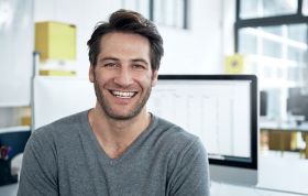 A cheerful man works on a computer, representing the MCSA Windows Server 2016 Online course in a professional setting.