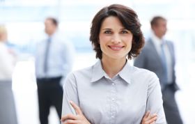 A woman smiles warmly, standing before a group, representing the MCSE SharePoint 2013 course with engagement and positivity.
