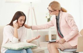 Woman discussing mental health with female doctor on couch, representing Mental Health Awareness in a supportive care environment.