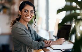 Smiling woman at desk working on laptop, embodying focus and positivity for Mental Health Support Champion Online course.