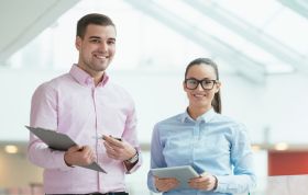 Man and woman in glasses smiling and holding clipboard, representing the Microsoft Access 2010 Course for database management skills.